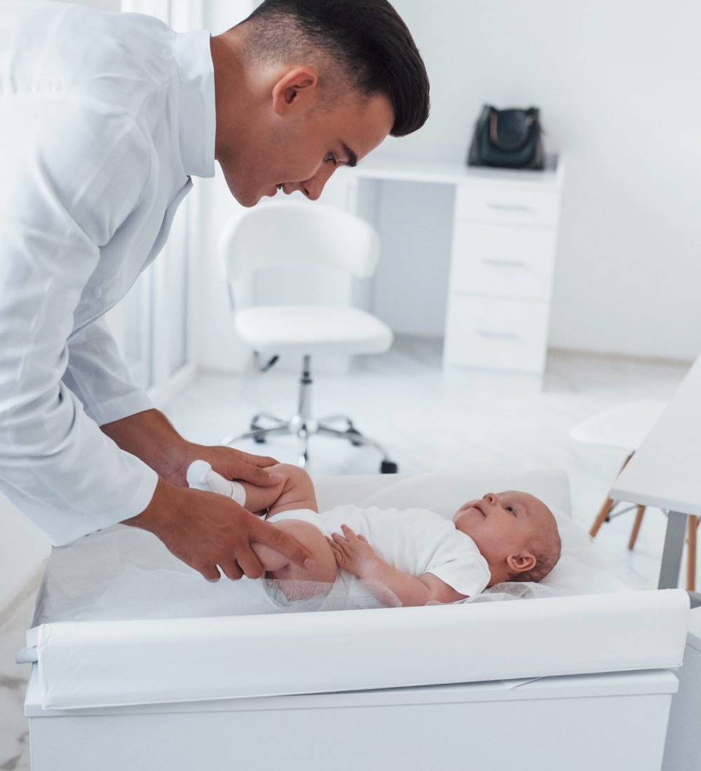 Young pediatrician is with little baby in the clinic at daytime.